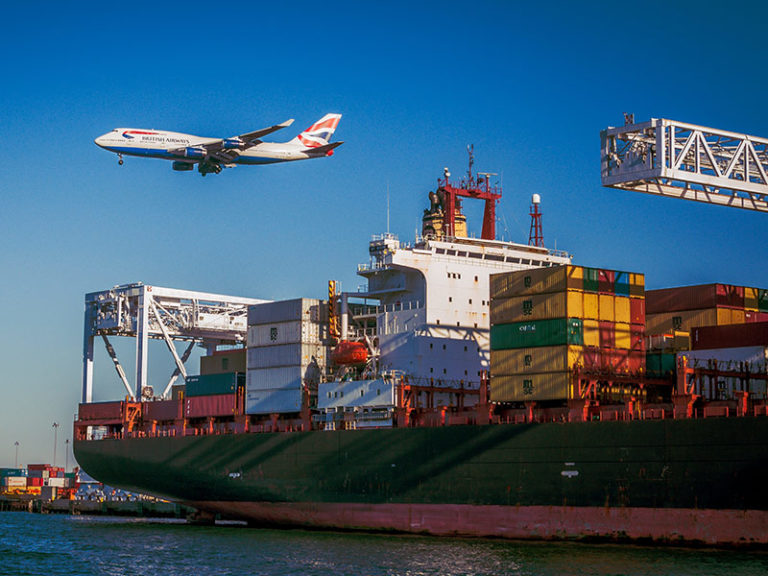 an airplane flying over a large freight ship