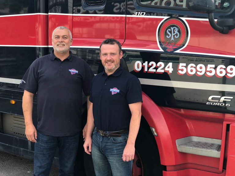 two men smiling with a truck behind them
