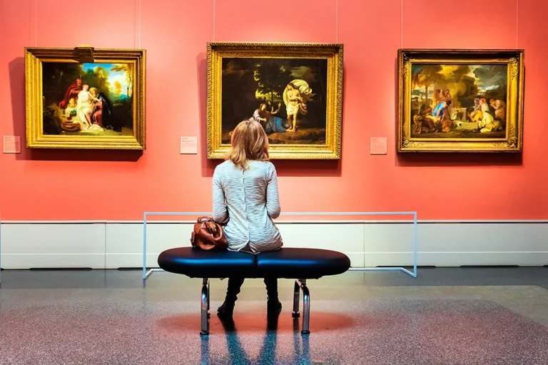 a woman sitting on a bench in an art museum observing some paintings on a wall