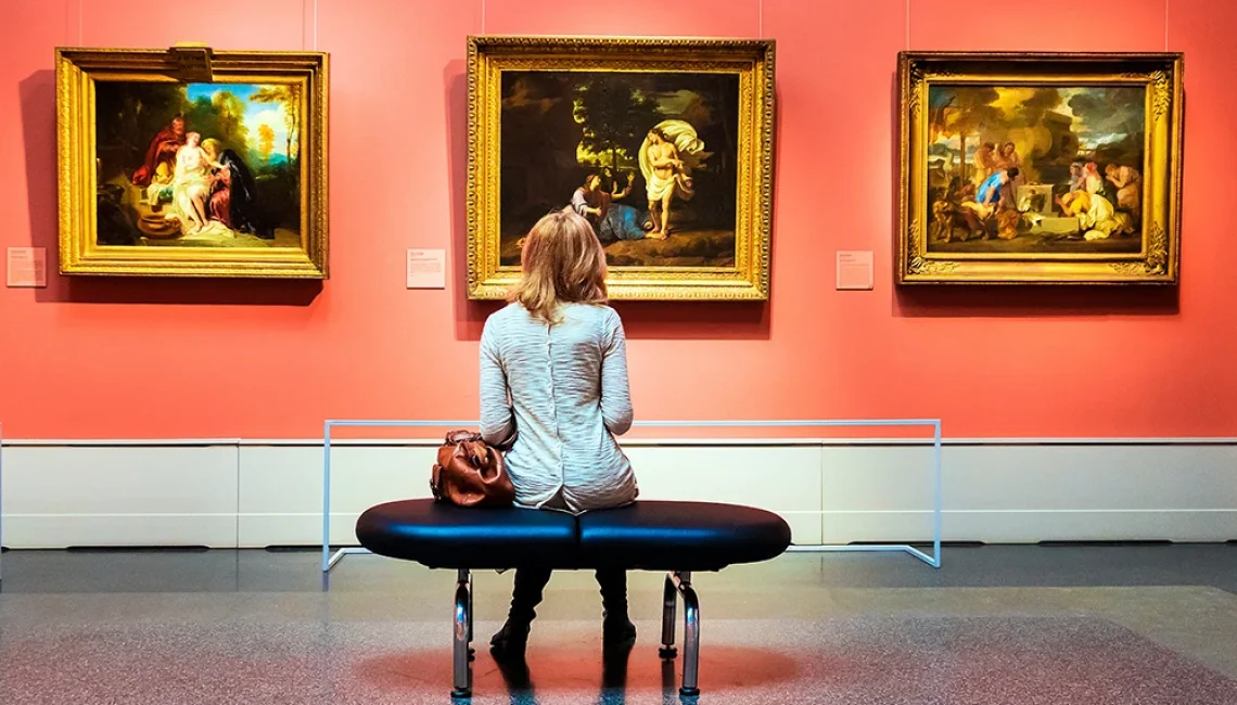 a woman sitting on a bench in an art museum observing some paintings on a wall
